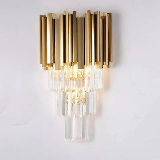 Bourbons Crystal Sconce illuminated on light grey wall, showing full profile with gold steel frame crown and three-tier cascading clear crystal drops glowing warmly