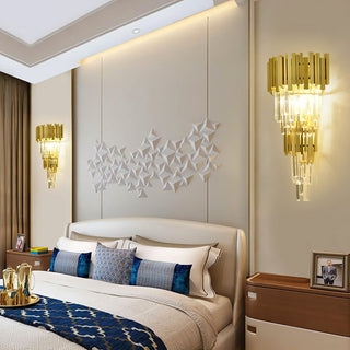 Two golden crystal wall sconces are mounted symmetrically on either side of the bed in the bedroom; the wall space between them features three-dimensional geometric decorative art, while the bed is adorned with blue and beige throw pillows.