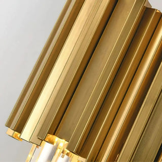 A close-up side view of a wall lamp's gold metal frame, showcasing the layered arrangement of wide, flattened metal tubes and their connection to the crystal elements at the base, with light radiating from within.