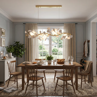 Ginkgo Vine linear chandelier hanging over a wooden dining table in front of a bright window by Vidir Lighting