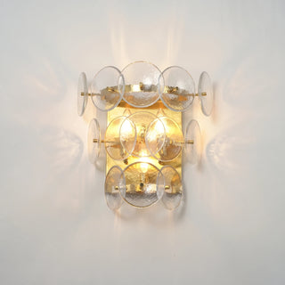 Lente Hammered Glass Disc Wall Sconce Vidirlighting Close-Up Lit View Showing Dramatic Radial Light Rays and Ambient Golden Halo on Wall